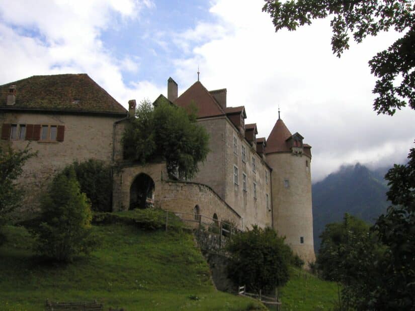 Situado em uma colina gramada, este castelo medieval de pedra com suas torres e arcos com portões ergue-se majestosamente em meio a árvores exuberantes e montanhas pitorescas, incorporando o fascínio atemporal típico dos pontos turísticos da Suíça.