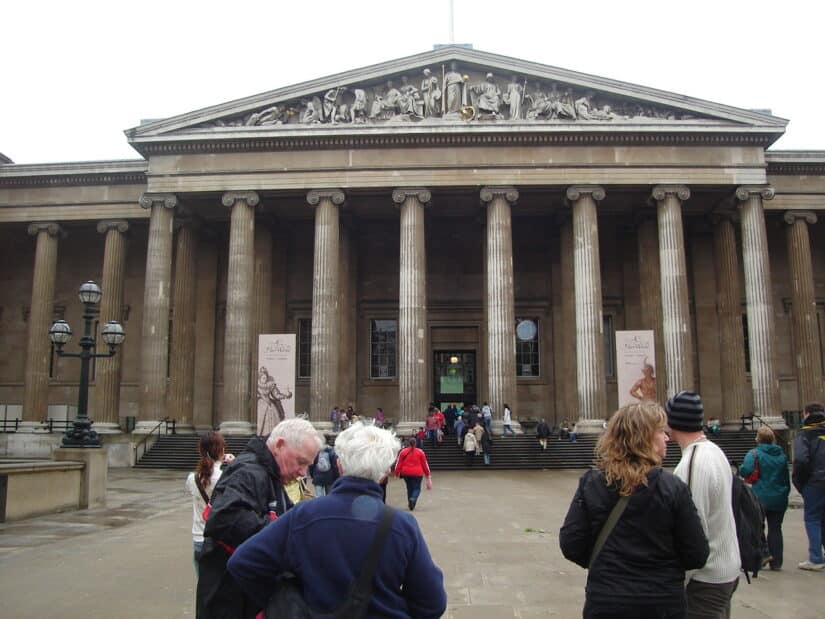 Pessoas se reúnem do lado de fora de um edifício histórico com colunas e esculturas detalhadas na fachada, frequentemente considerado uma das melhores atrações de Londres.