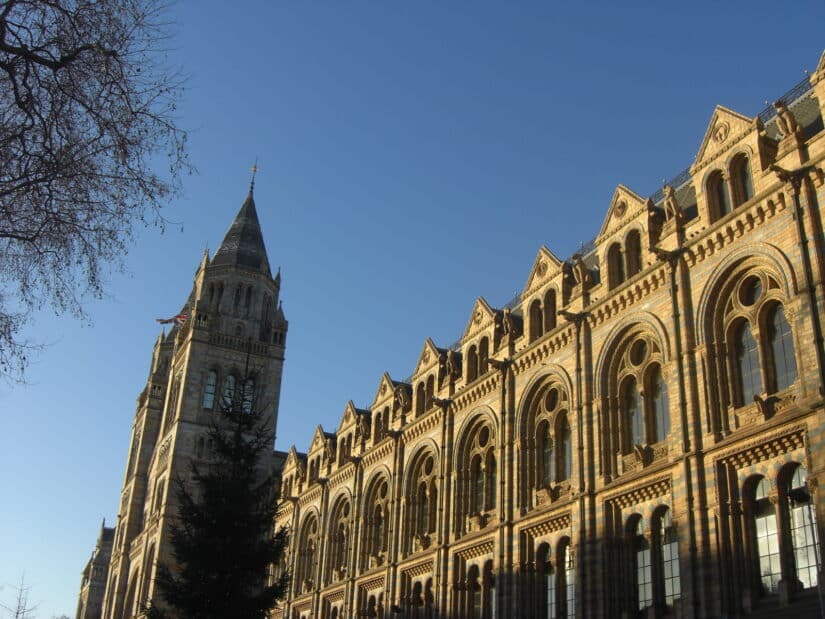 Um edifício histórico de tijolos com janelas em arco e uma torre alta sob um céu azul claro é uma das melhores atrações de Londres.