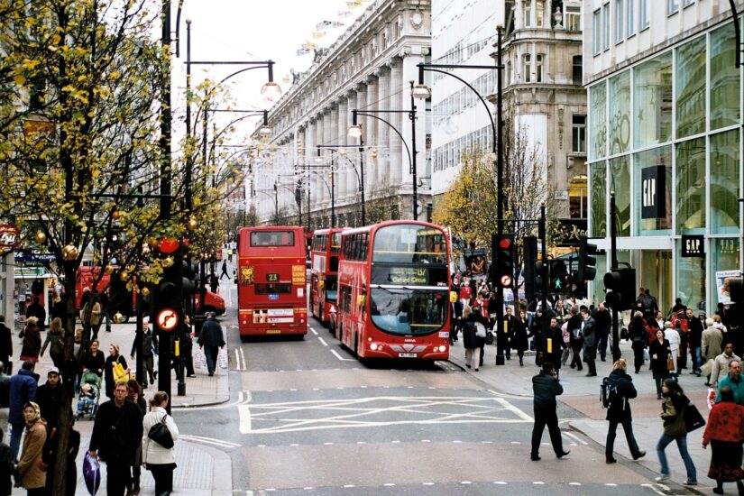 Uma movimentada rua da cidade com ônibus vermelhos de dois andares e pessoas atravessando, com lojas em ambos os lados, captura a essência de algumas das melhores atrações de Londres.