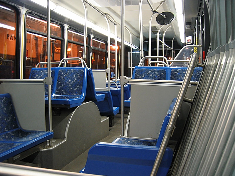 Dentro do ônibus noturno vazio do Aeroporto de Boston, assentos azuis e postes de metal brilham sob luzes fracas.