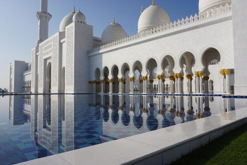 Mesquita branca com cúpulas espelhadas na piscina azul — perfeita para seus momentos de diversão em Abu Dhabi.
