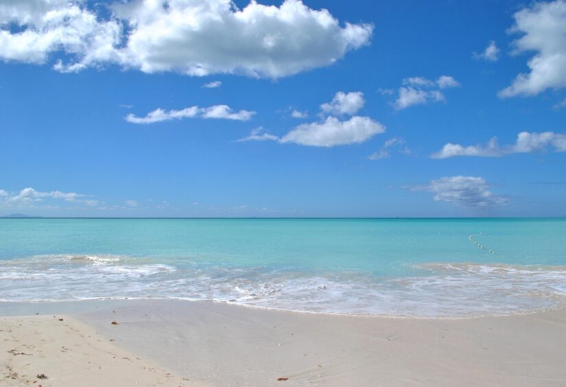 Praia de areia com ondas suaves, água azul-turquesa e um céu brilhante — ideal para uma escapada seguro viagem em Antígua e Barbuda.