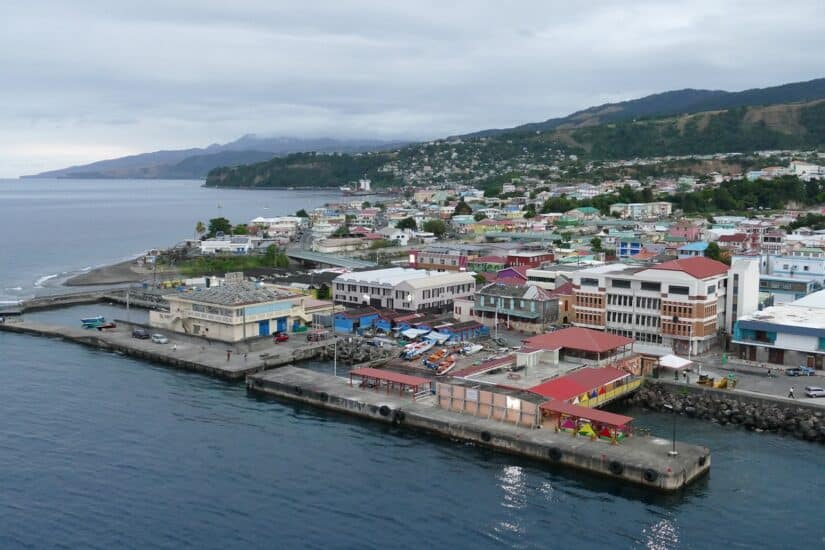 Vista aérea de uma cidade costeira em Dominica — edifícios coloridos, colinas verdes e seguro viagem para Dominica recomendado.