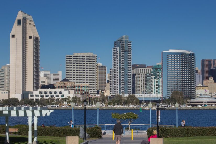Pessoas caminham perto da água apreciando o horizonte de San Diego — ideal para quem planeja uma viagem segura para San Diego.