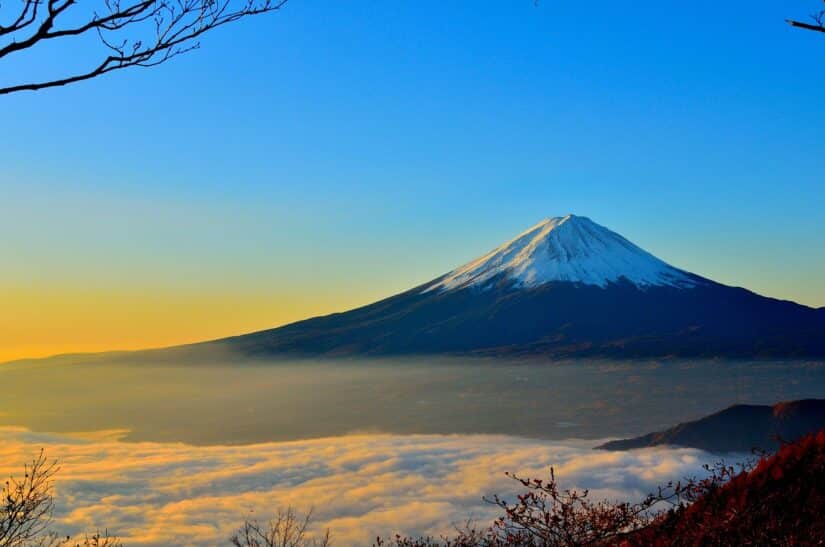 Monte Fuji coberto de neve ao nascer do sol, nuvens abaixo, céu limpo acima — um sonho para qualquer viajante.