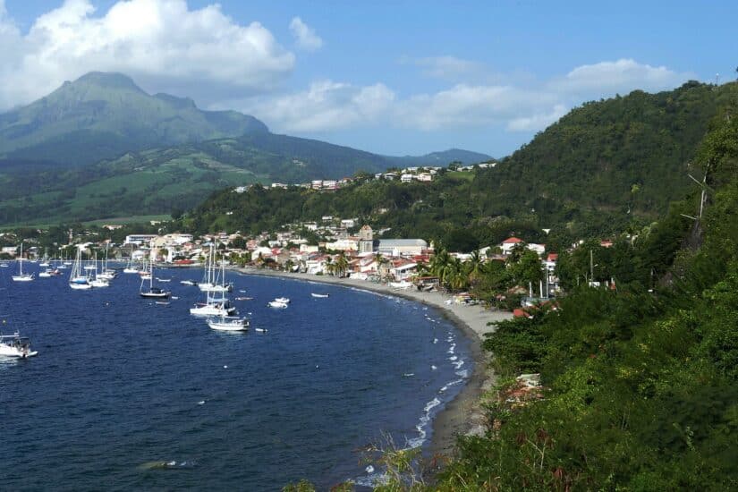 Barcos ancorados ao longo da costa curva da Martinica, com colinas verdes e uma montanha – lembre do seguro viagem para Martinica.