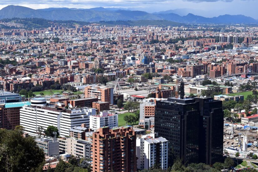 Vista aérea de uma extensa paisagem urbana com vários edifícios, montanhas e hotéis na Zona Rosa desaparecendo no céu parcialmente nublado.