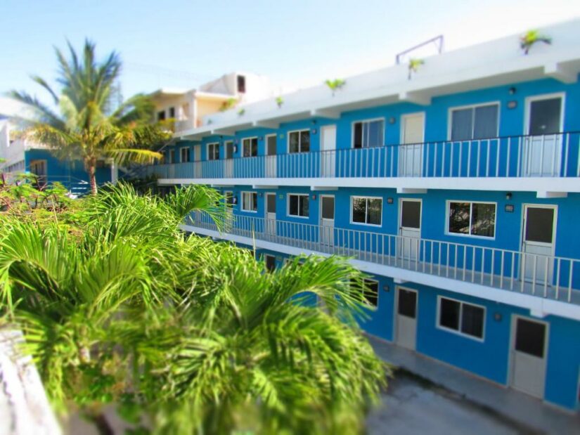 Charmoso edifício azul de três andares com varandas cercadas por palmeiras exuberantes, perfeito para quem busca hotéis baratos em Cancún.