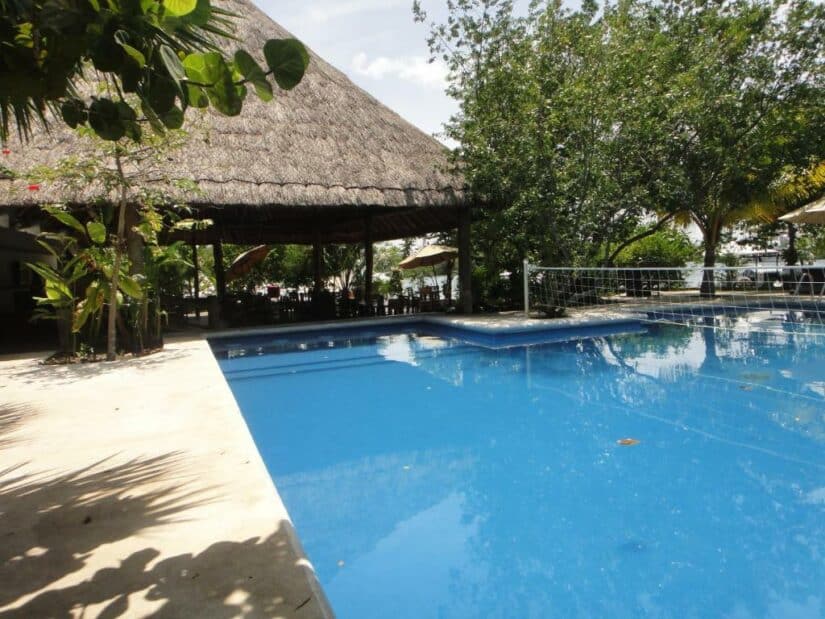 Um retiro tropical com piscina ao ar livre, gazebo com telhado de palha e árvores exuberantes, ideal para quem busca hotéis baratos em Cancún.