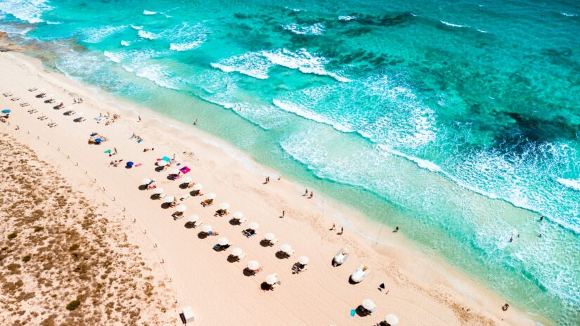 melhores hotéis em Figueretas nas Ilhas Baleares Vista aérea de onde ficar em Ibiza: praia de areia com guarda-sóis e pessoas junto a ondas azul-turquesa.