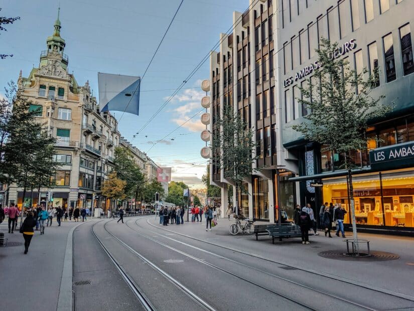 hotéis na Bahnhofstrasse na Suíça para compras Rua movimentada da cidade com trilhos de bonde, pessoas caminhando e árvores - perfeita para explorar onde ficar em Zurique.