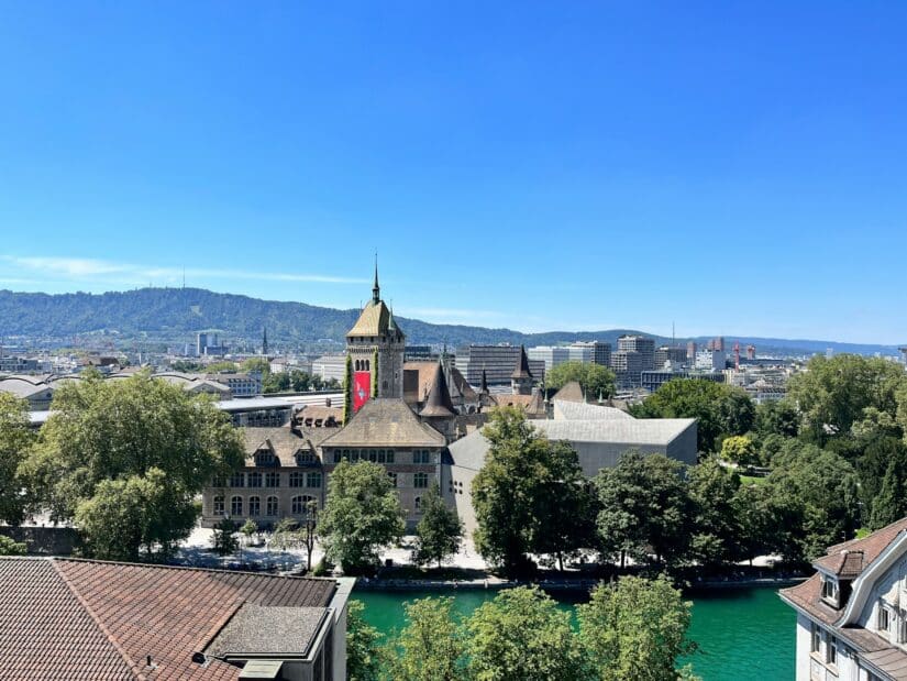 hotéis em Zurich West na Suíça Uma paisagem urbana cênica com uma torre de relógio, árvores e rio - perfeita para descobrir onde ficar em Zurique.