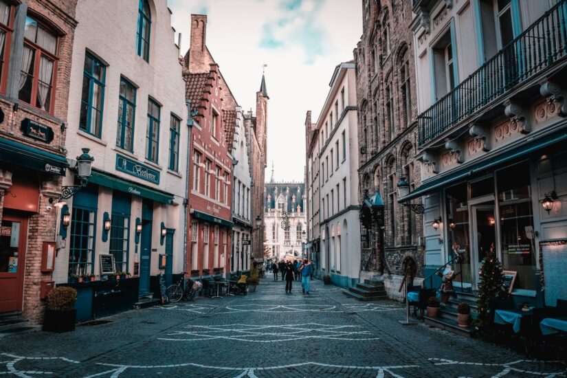 onde ficar em Bruges perto da Steenstraat na Bélgica Uma rua de paralelepípedos repleta de prédios históricos sugere hotéis na Bélgica enquanto as pessoas caminham em direção a uma igreja distante.