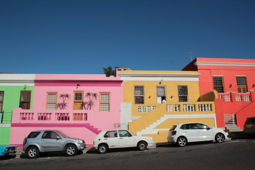 onde ficar em Cape Town no bairro Bo-Kaap na África do Sul Casas de cores vivas em rosa, amarelo e vermelho - perfeitas para quem procura hospedagem na Cidade do Cabo sob um céu azul claro.
