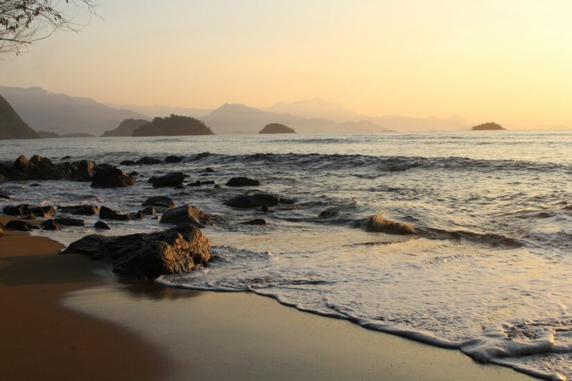 onde ficar em Paraty na Praia do Pontal Ondas que se espalham na PRaia do Pontal ao pôr do sol, capturando a beleza com montanhas distantes.