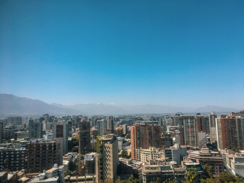 Melhores hotéis em santiago central no chile Um horizonte de cidade com prédios altos, onde ficar em Santiago, sob um céu azul claro e montanhas distantes.