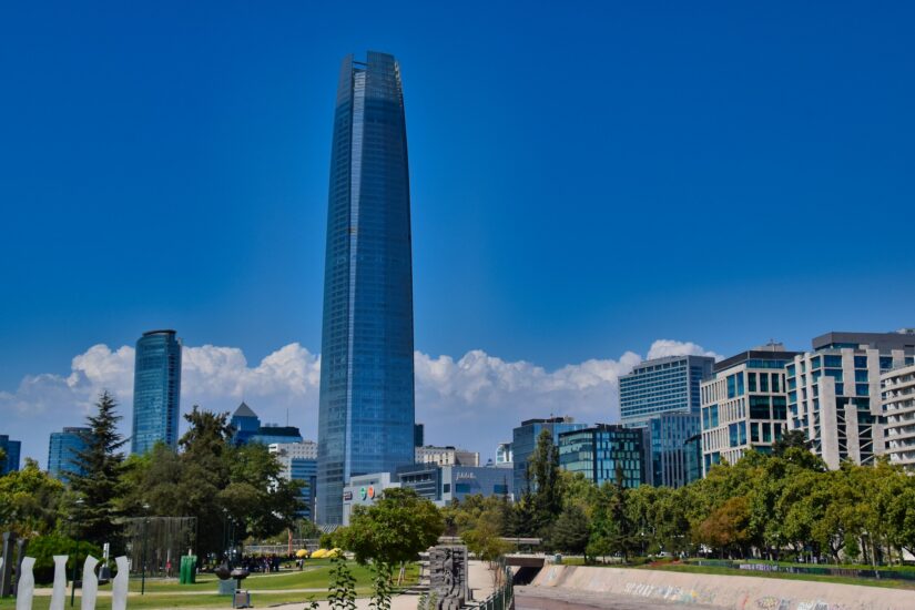 hotéis em Providencia no Chile Arranha-céus de vidro, edifícios modernos e vegetação e o incrível Sky Costanera - explore onde ficar em Santiago sob um céu azul claro.