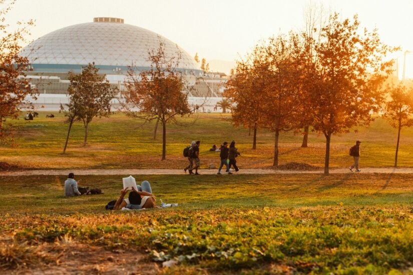 onde ficar em Santiago no bairro Vitacura no Chile. Pessoas relaxando em um parque com árvores de outono perto de um edifício abobadado ao pôr do sol - perfeito conhecer o Chile.