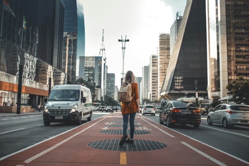 melhores hotéis perto da avenida paulista Uma mulher na Avenida Paulista com uma mochila explora onde ficar em São Paulo, caminhando por uma rua da cidade repleta de prédios altos.