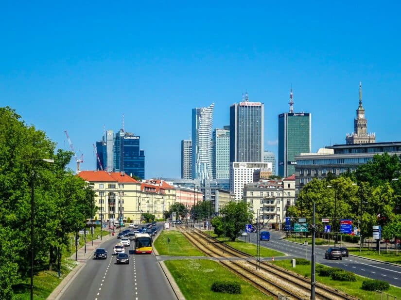 melhores hotéis no bairro Wola na Polônia Uma rua da cidade em onde ficar em Varsóvia, com carros, trilhos de bonde, árvores e arranha-céus modernos sob um céu azul claro.
