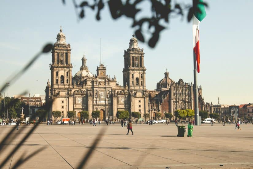 Melhor bairro para brasileiros no México A Catedral Metropolitana da Cidade do México sob a luz do sol, onde ficar na Cidade do México, e uma grande bandeira mexicana nas proximidades.