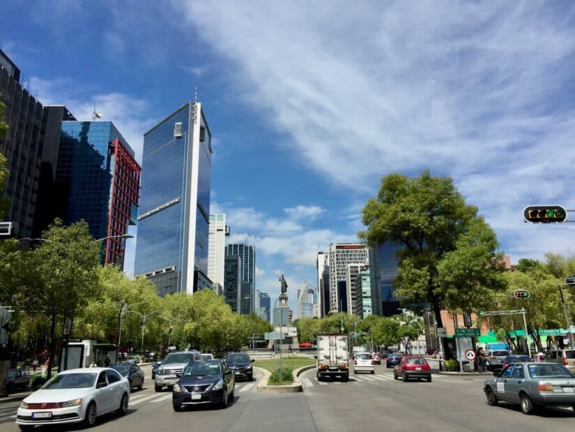 onde ficar na Cidade do México na Avenida PAseo de la Reforma Ampla rua da cidade com carros, prédios altos, árvores e uma estátua - perfeita para explorar CDMX