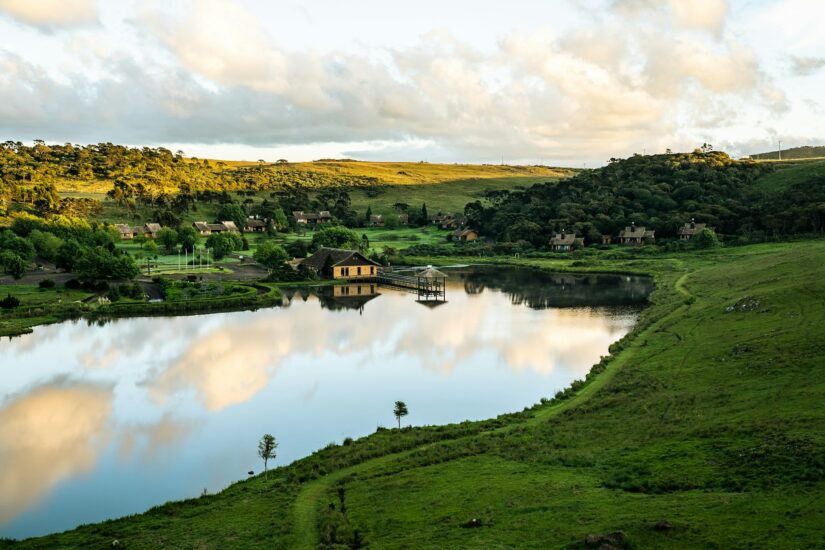 melhores hotéis em Gaspar em Santa Catarina Uma casa à beira do lago com reflexos, ideal para quem busca onde ficar no Vale Europeu na cidade de Gaspar, cercada por colinas e céu nublado.