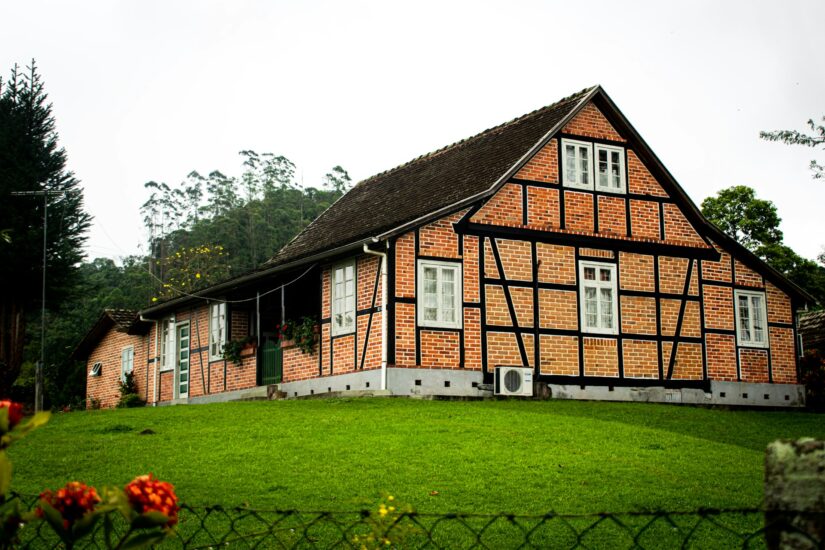 melhores hotéis em Pomerode em Santa Catarina Casa de tijolos e madeira com janelas verdes em Pomerode, ideal para onde ficar no Vale Europeu, situada em uma colina gramada com árvores atrás.