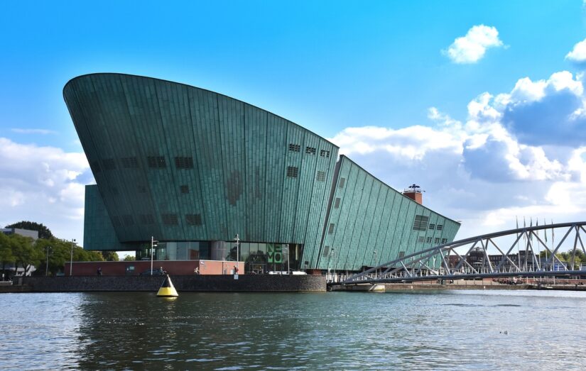 Moderno edifício verde com telhado inclinado perto da água - um local ideal para onde ficar em Amsterdã.