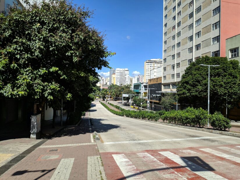 onde ficar em Belo Horizonte no bairro Funcionários Rua ensolarada no bairro Funcionários em BH com prédios altos, árvores e calçadas vazias sob um céu azul claro.