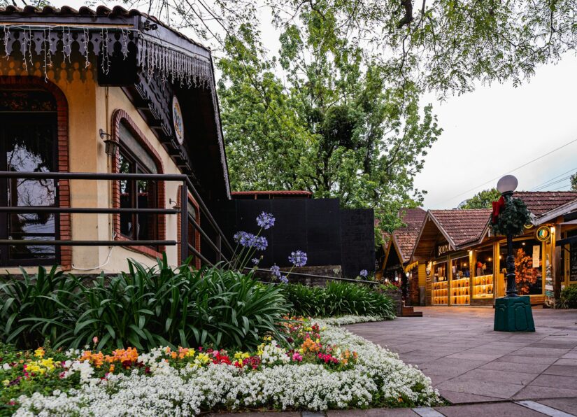 melhores hotéis no bairro Bavária na serra gaúcha Uma rua charmosa em onde ficar em Gramado, com canteiros de flores, árvores e prédios rústicos decorados com luzes e letreiros.