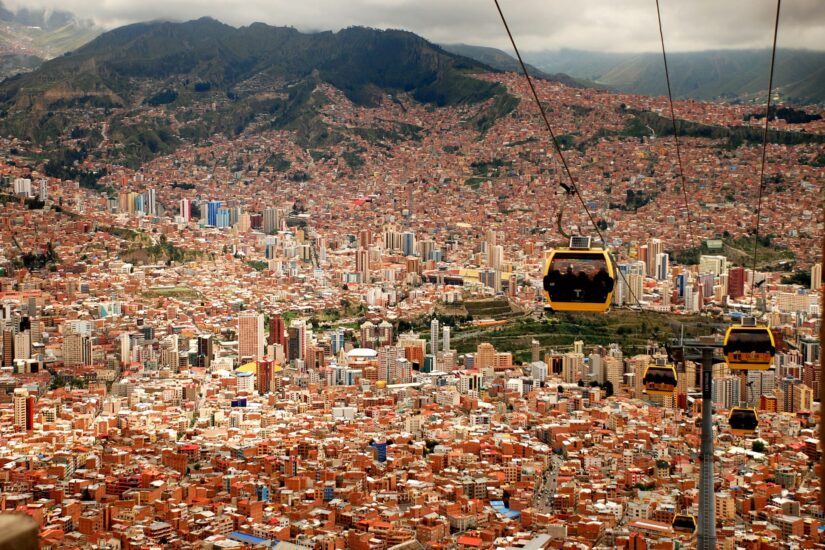 hotéis baratos no centro da capital da Bolívia Vista aérea de onde ficar em La Paz no centro, com prédios coloridos e teleféricos sobre a cidade em um cenário de montanhas.