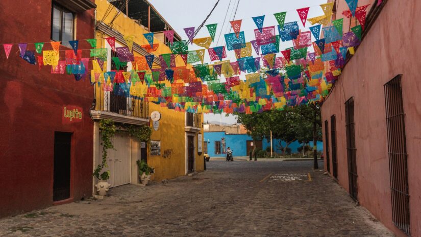 Faixas coloridas de papel picado penduradas em uma rua de paralelepípedos - uma visão convidativa para quem procura onde ficar em Oaxaca.