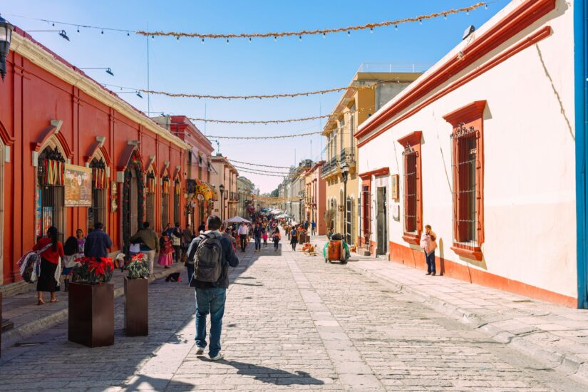As pessoas passeiam por uma rua colorida repleta de lojas em Oaxaca - descubra onde ficar em Oaxaca - sob luzes de cordas festivas.