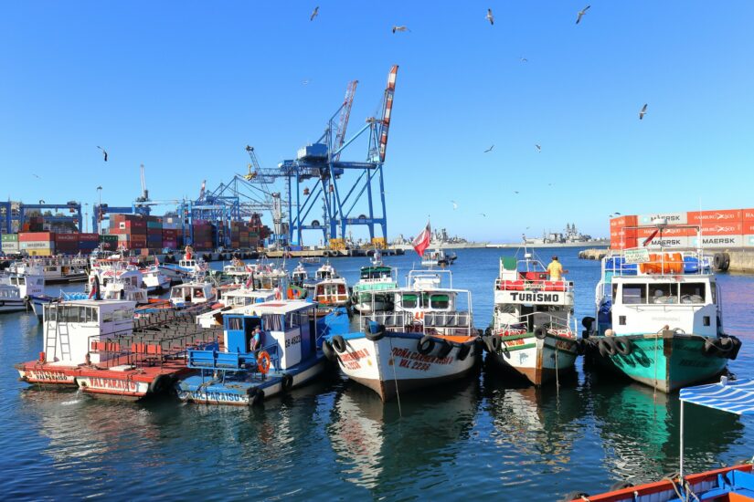 Melhores hotéis no Barrio Puerto perto de Viña del Mar Pequenos barcos atracados no Porto Muelle Prat, contêineres de transporte além das vistas clássicas de onde ficar em Valparaíso sob um céu azul.