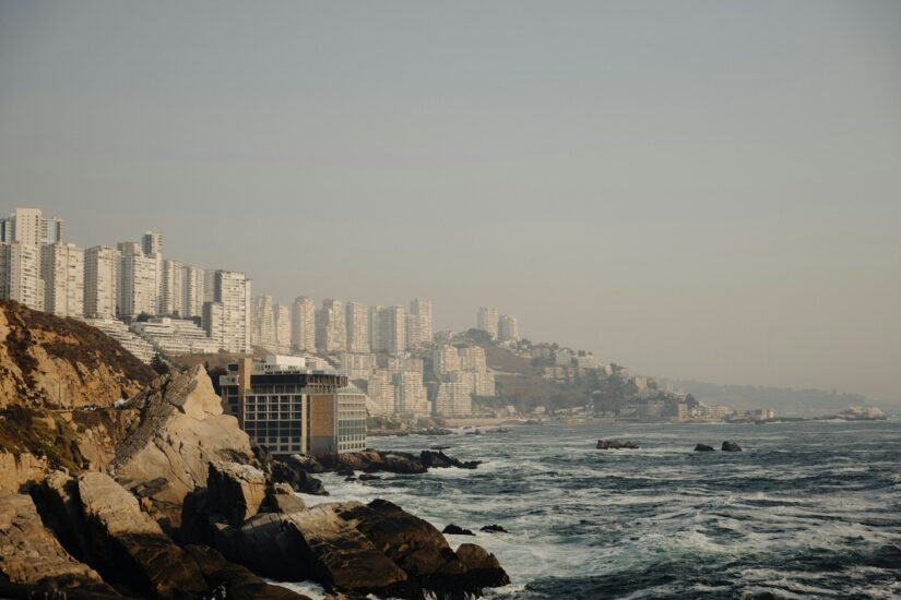 onde ficar em Valparaíso perto da Playa Ancha no Chile Prédios altos se alinham em uma costa rochosa do Cerro Playa Ancha no Chile enquanto as ondas quebram sob um céu nebuloso.