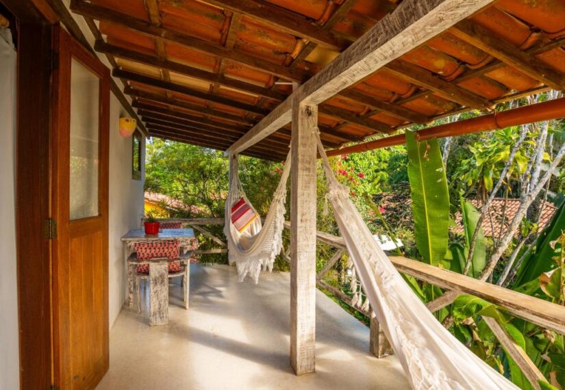 Varanda sombreada com duas redes, uma pequena mesa, cadeiras e plantas exuberantes - perfeita para onde ficar em Trancoso.