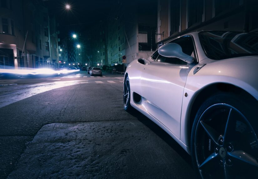 melhores hotéis no Design District em Helsinque na Finlândia Um carro esportivo branco estacionado em uma rua de Design District à noite, como aqueles perto de onde ficar em Helsinque, com luzes borradas atrás.