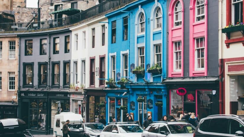 Prédios coloridos se alinham em uma rua movimentada em Edimburgo, onde carros estacionados e pedestres agitados criam uma cena animada, talvez enquanto procuram o melhor chip de celular em Edimburgo.
