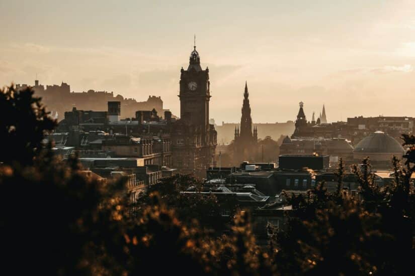 Horizonte da cidade de Edimburgo ao pôr do sol, com uma torre do relógio e silhuetas de edifícios históricos, que lembram o charme atemporal encontrado ao explorar Edimburgo para comprar um chip de celular.