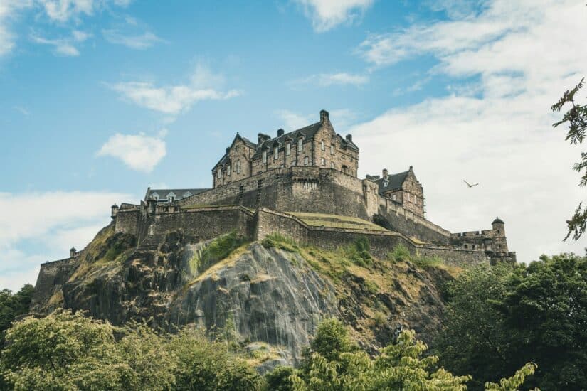 Um castelo medieval de pedra situado no topo de uma colina rochosa sob um céu parcialmente nublado, cercado por uma vegetação exuberante, oferece um local perfeito para explorar enquanto você usa seu chip de celular em Edimburgo para capturar e compartilhar sua beleza atemporal.