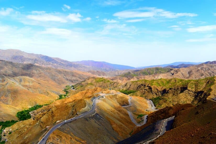 Uma estrada sinuosa através de uma paisagem árida e montanhosa sob um céu azul brilhante com nuvens dispersas ecoa o espírito aventureiro de viajar com um chip de celular na África para permanecer conectado.