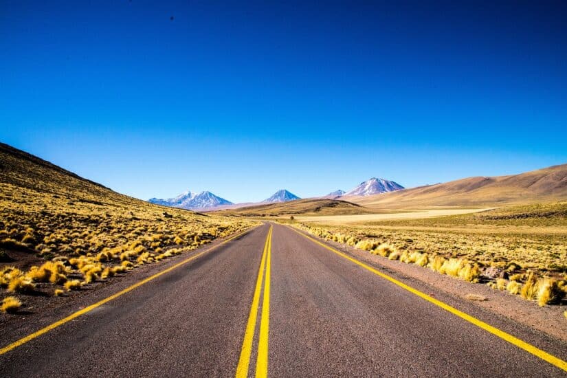 Estrada aberta para montanhas distantes sob um céu azul claro na paisagem desértica do Chile, perfeita para viajantes conectados com Holafly.