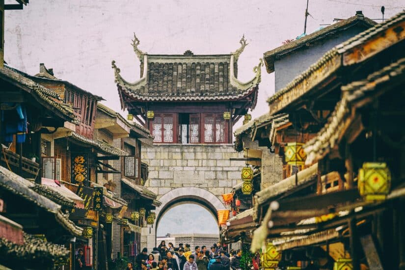 Rua movimentada em uma antiga cidade chinesa com vistas da China Holafly, arquitetura tradicional e um arco ao fundo.