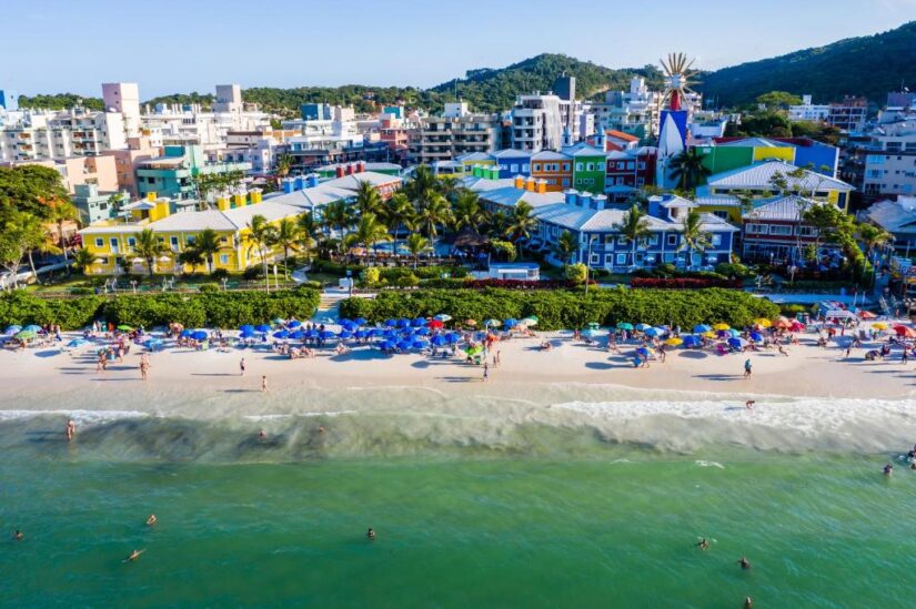 melhores hotéis e pousadas na Praia da Bombinhas SC Vista aérea de uma cidade colorida à beira-mar - Onde ficar em Bombinhas para praias vibrantes e diversão animada à beira-mar.