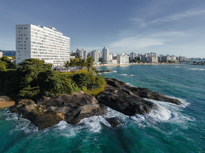 onde ficar em Guarapari na Praia Areia Preta no Espirito Santo Edifício branco em uma costa rochosa com ondas, paisagem urbana e arranha-céus no Espírito Santo sob um céu claro.
