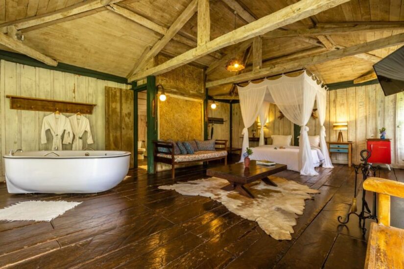 melhores pousadas no interior de Minas Gerais Interior de cabine de madeira rústica - ideal para onde ficar em Ibitipoca, em Minas Gerais - com cama de dossel, banheira, assentos aconchegantes e iluminação aconchegante.