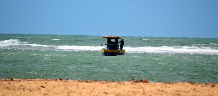melhores hotéis e pousadas na Praia do Marceneiro em Alagoas Um pequeno barco com um dossel flutua na Praia do Marceneiro, perto de onde ficar em São Miguel dos Milagres em um mar agitado sob um céu azul claro.
