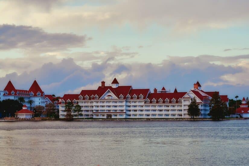 Grande resort branco com telhados vermelhos em um lago calmo sob um céu nublado ao pôr do sol perto da Disney